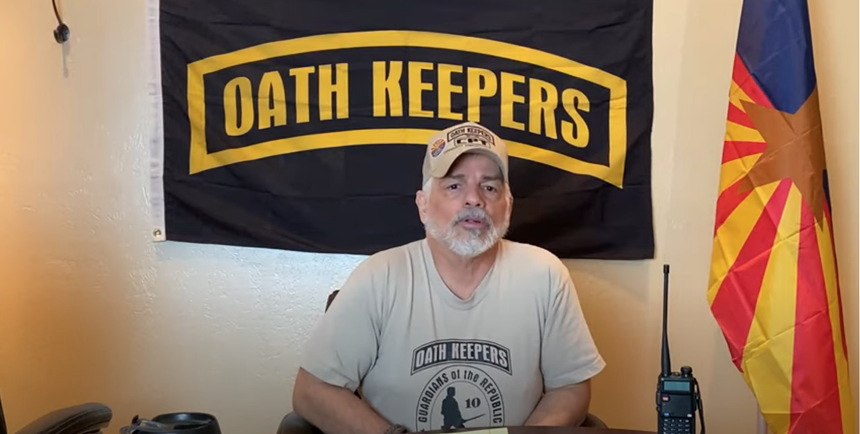a man in front of an oath keepers flag