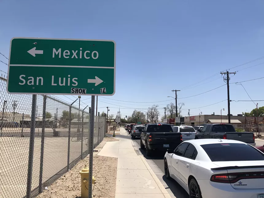cars waiting on a street near a sign that says Mexico to the left, san luis to the right