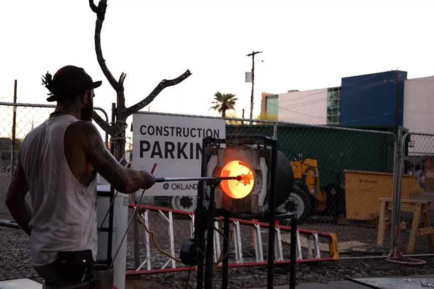 a man sticks a glass-blowing pipe into a furnace