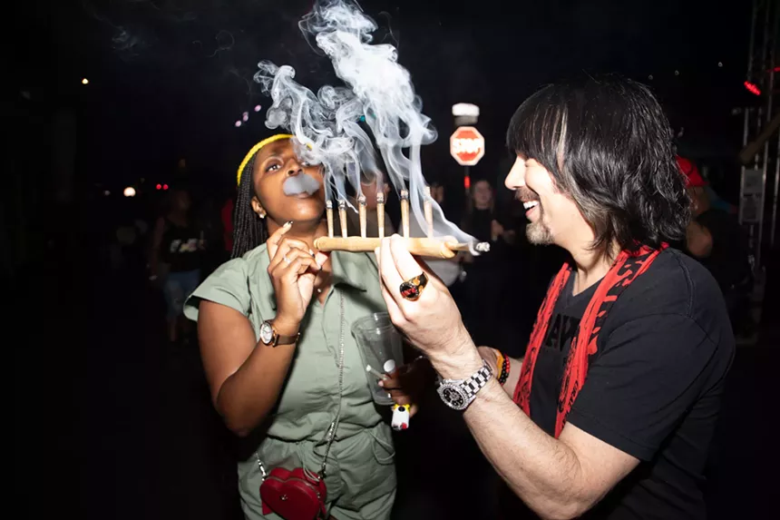 josh kesselman holds a flute pipe while a woman blows smoke out of her mouth next to him