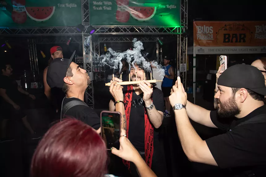 josh kesselman holds a flute pipe while one man smokes and another films on his phone