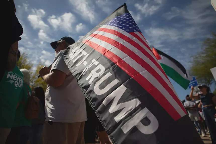 a man holds a flag with the American flag and the words "anti-trump"
