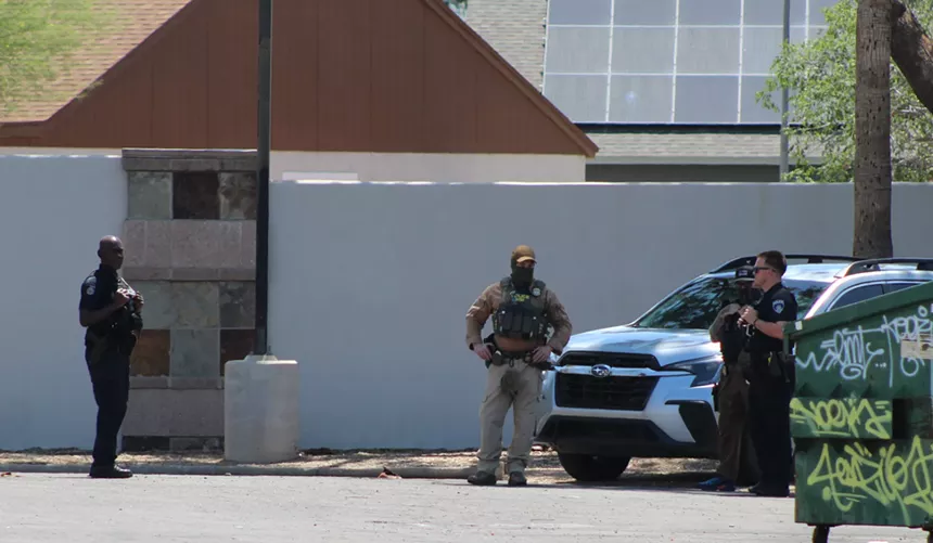 Police officers and a masked agent from Homeland Security Investigations mill about the back lot off a Walmart Neighborhood Market after an immigration raid Tuesday morning.