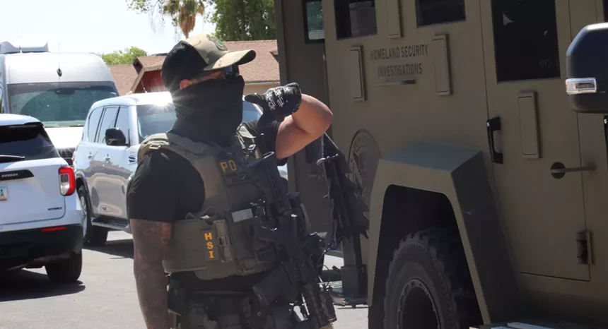 a masked HSI agent with a rifle near an armored truck