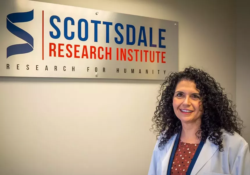 a woman in a lab coat stands in front of a sign for Scottsdale Research Institute