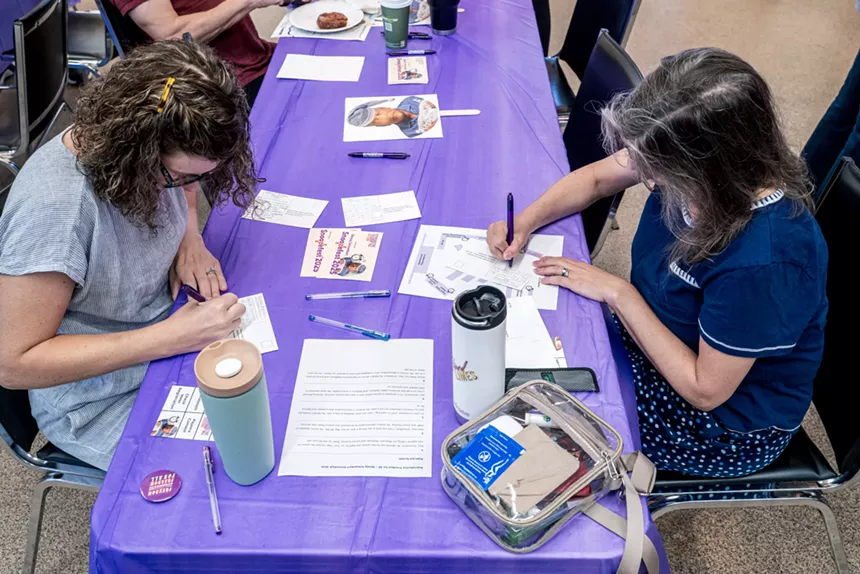 two women write messages on a pile of postcards