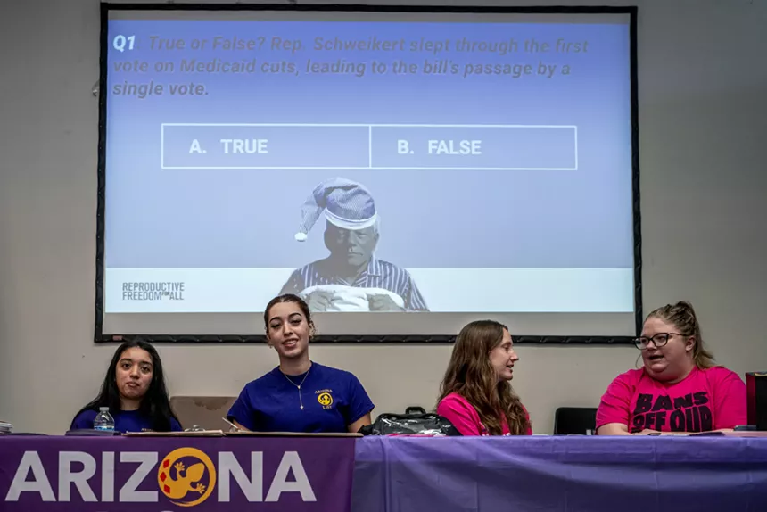 women sit at a table below a screen
