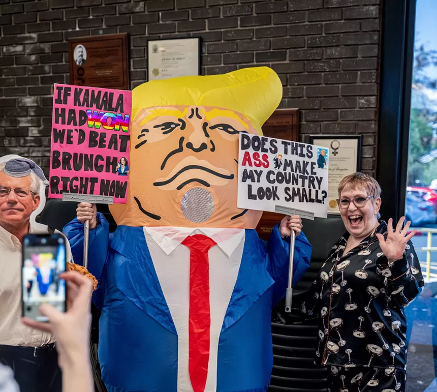 an inflatable donald trump poses with two women