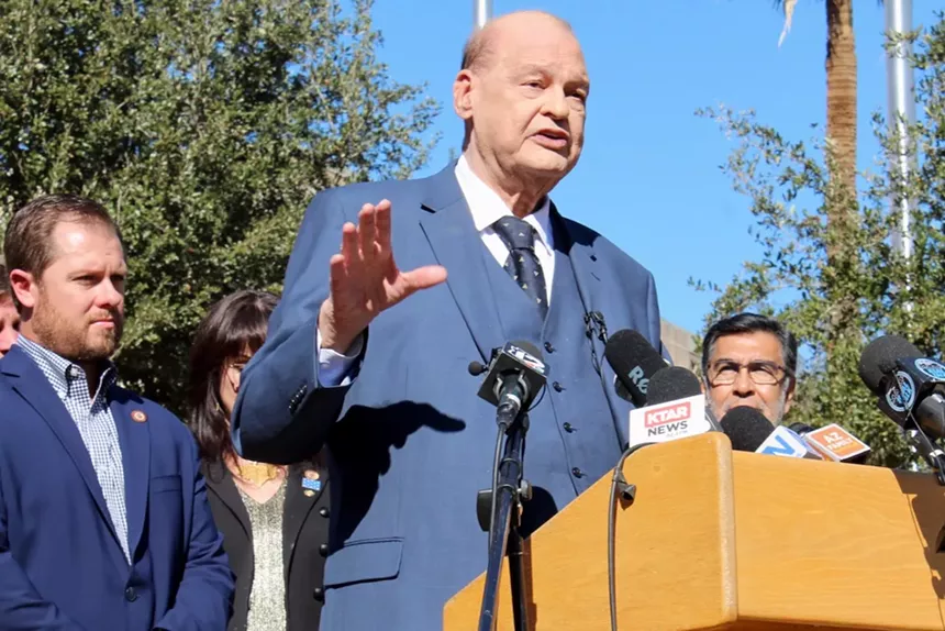 tom horne speaks at a press conference with jake hoffman standing behind him