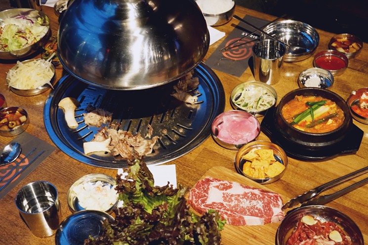 Various side dishes, kimchi jjigae, rice, and lettuce leaves for wrapping surround the meat at the grilling table in Sizzle Korean Barbecue in Phoenix. - MEAGAN MASTRIANI