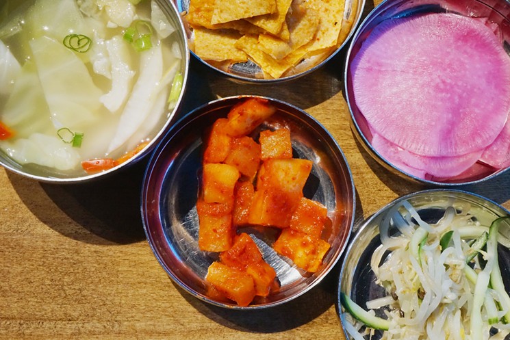 Side dishes at Sizzle Korean Barbecue in Phoenix may include radish kimchi (center), as well as cold soup, fish cakes, pickled radish discs, and sautéed bean sprouts (clockwise from left). - MEAGAN MASTRIANI