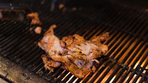 The marinated pork is par-cooked on a wood-burning grill. - SHELBY MOORE