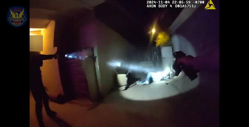 Image: body camera footage showing arms pointing a gun at a suspect on the ground in a spotlight at night