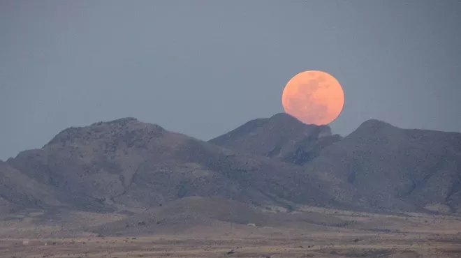 A full moon in the sky over mountains.