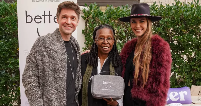 Image: a man and woman pose with whoopi goldberg, who is holding a gray pouch that says "Better U"